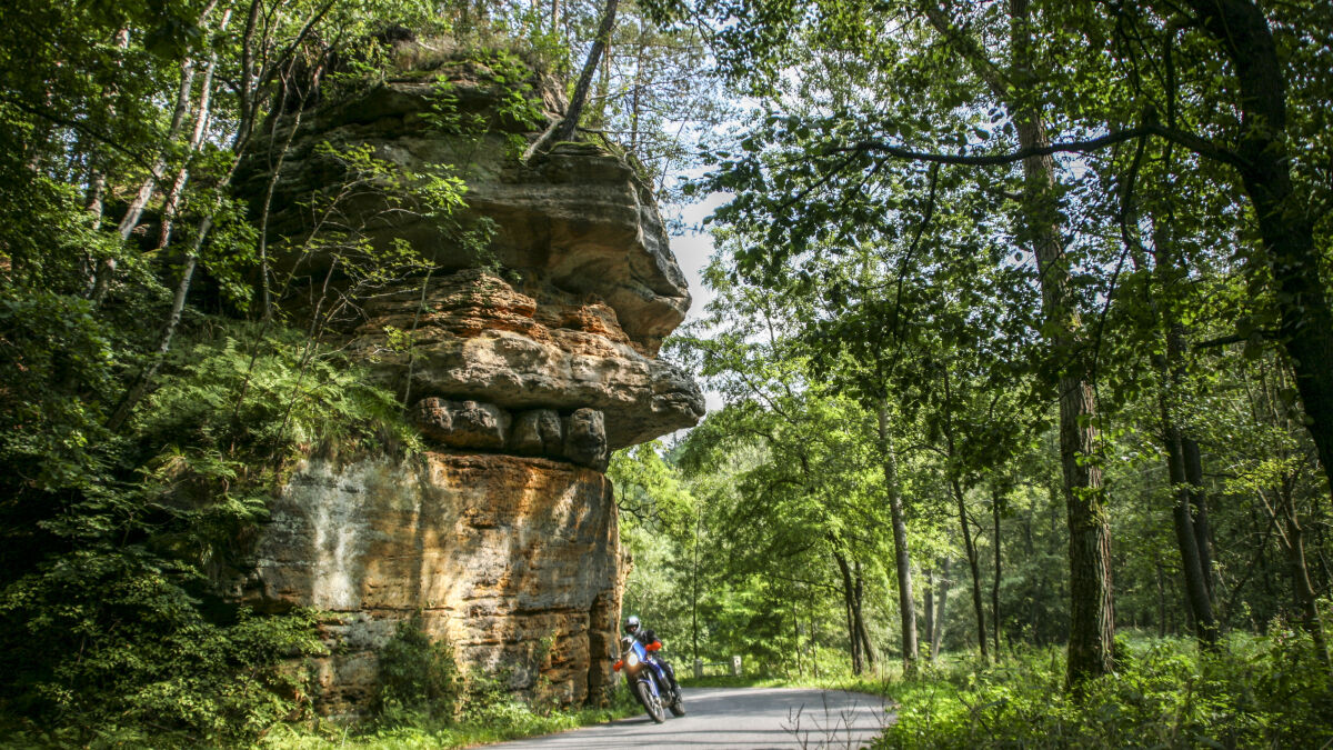 Sandsteinfelsen überragt eine Waldstraße, darunter ein Motorrad in der Kurve Sandsteinfelsen überragt eine Waldstraße, darunter ein Motorrad in der Kurve